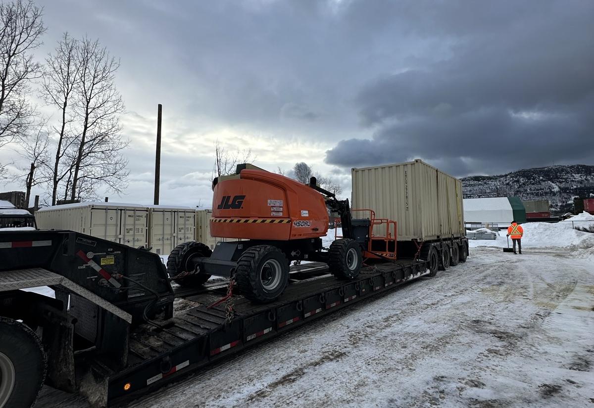 A boom lift and a sea can loaded on a lowboy for the run north