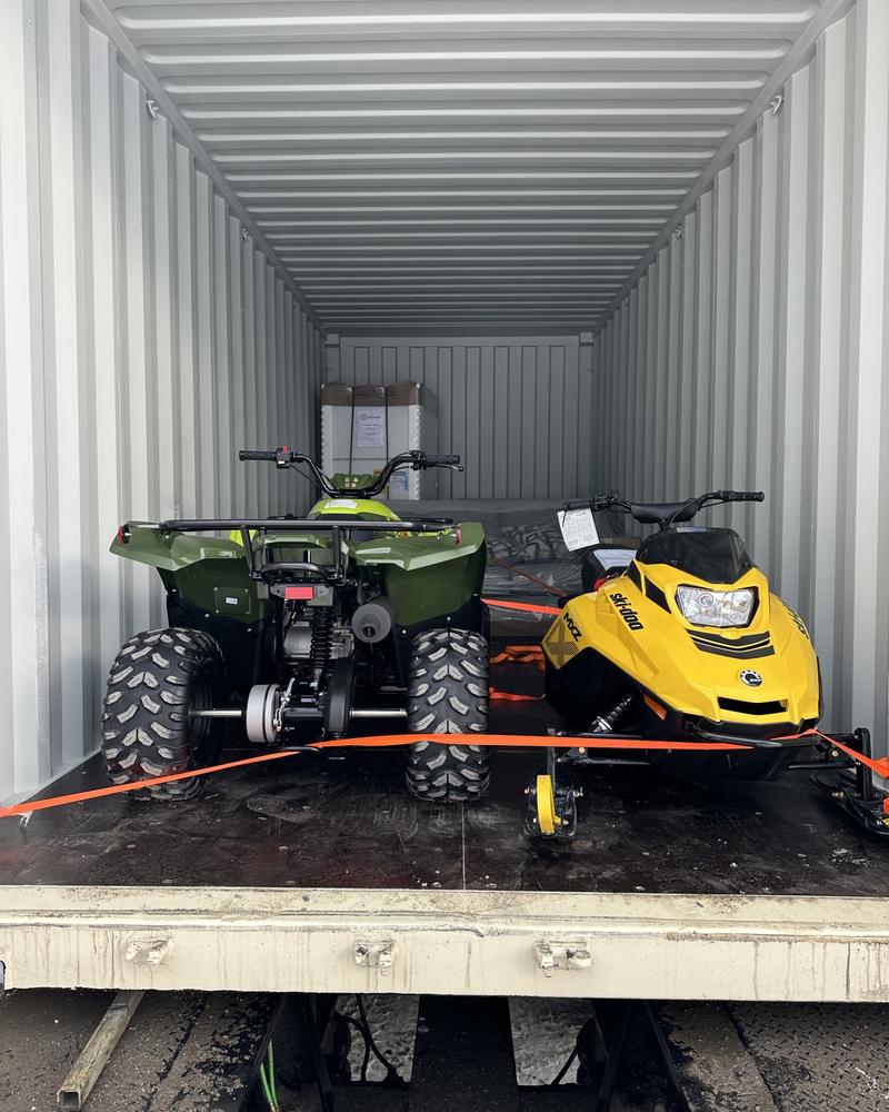An ATV and a snowmobile strapped down inside a sea can